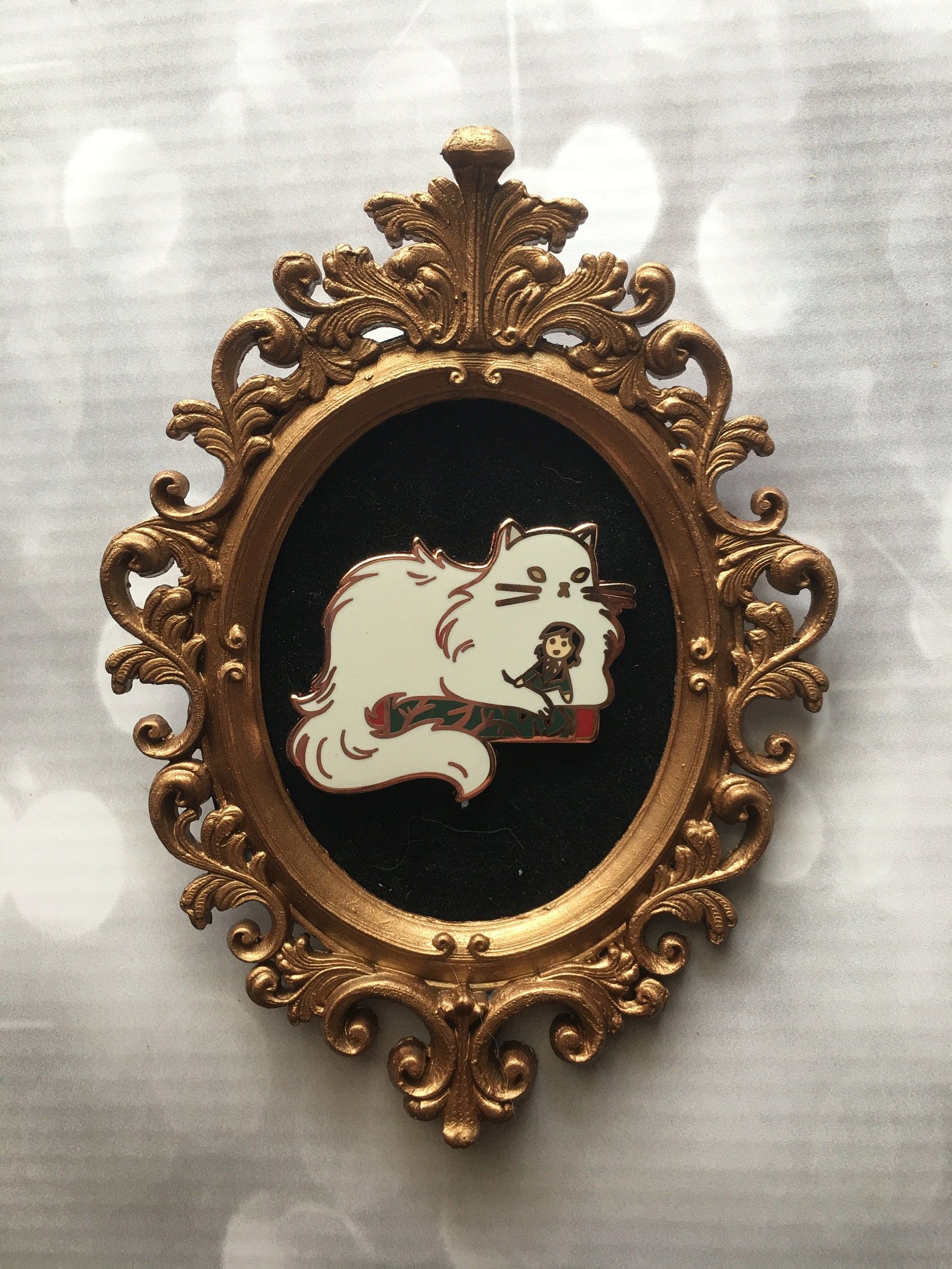 An enamel pin of a fluffy white cat and a small girl