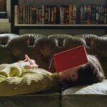 a photo of a woman lying on a couch with an open book resting on her face