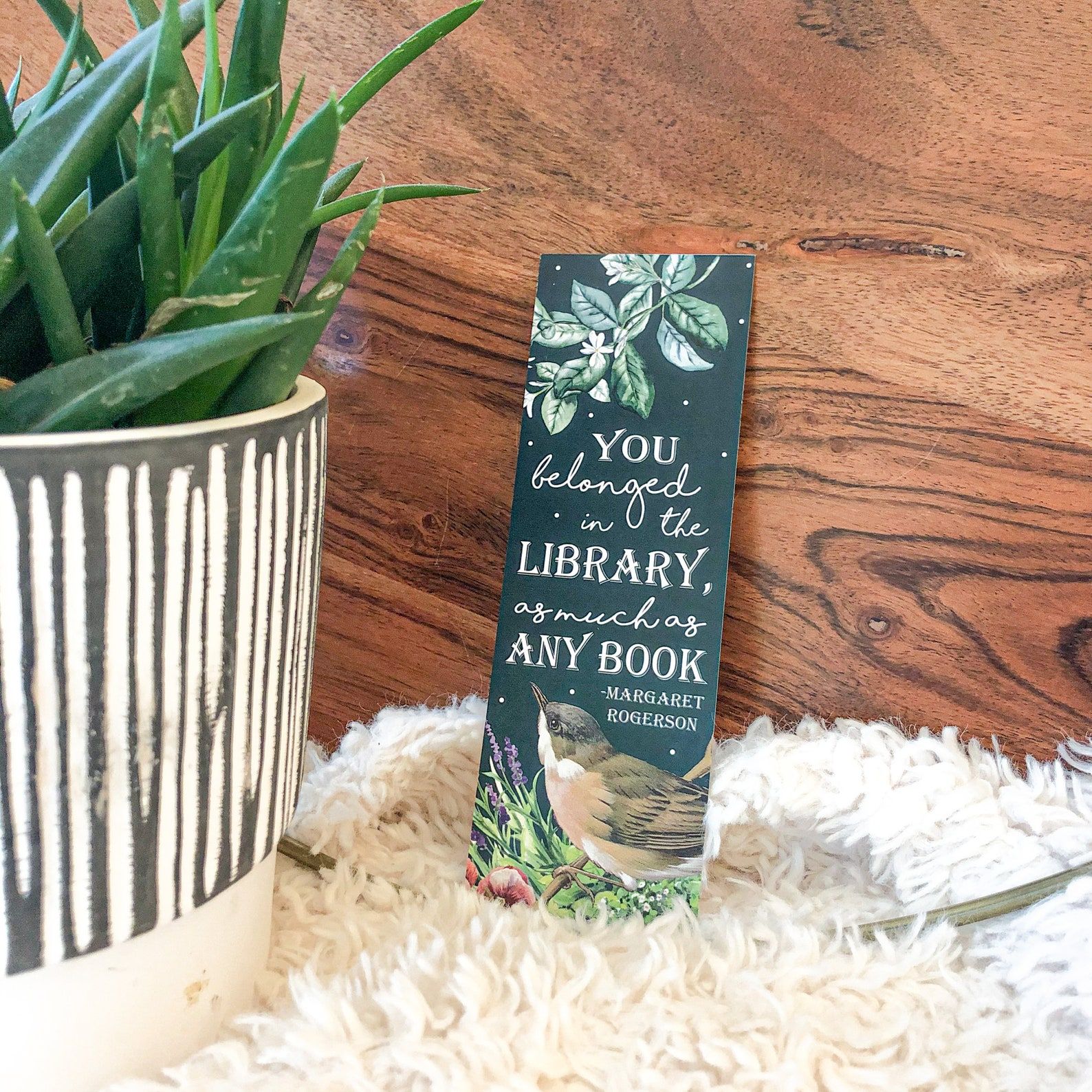 A blue bookmarks that reads "You belonged in the library, as much as any book" with an illustration go a bird
