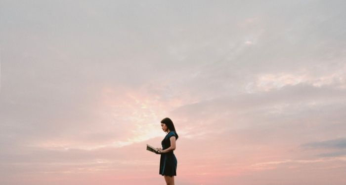 young woman reading book, pink sky