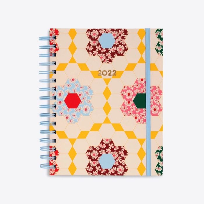 a small notebook in a hexagonal floral and light pink patchwork pattern. The floral patchwork is in light blue bright pink, green, and dark red patterns