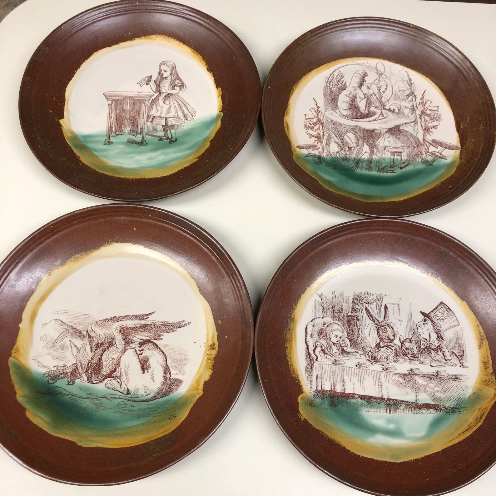 Four ceramic plates with brown rims and painted images from Alice in Wonderland in their centers.
