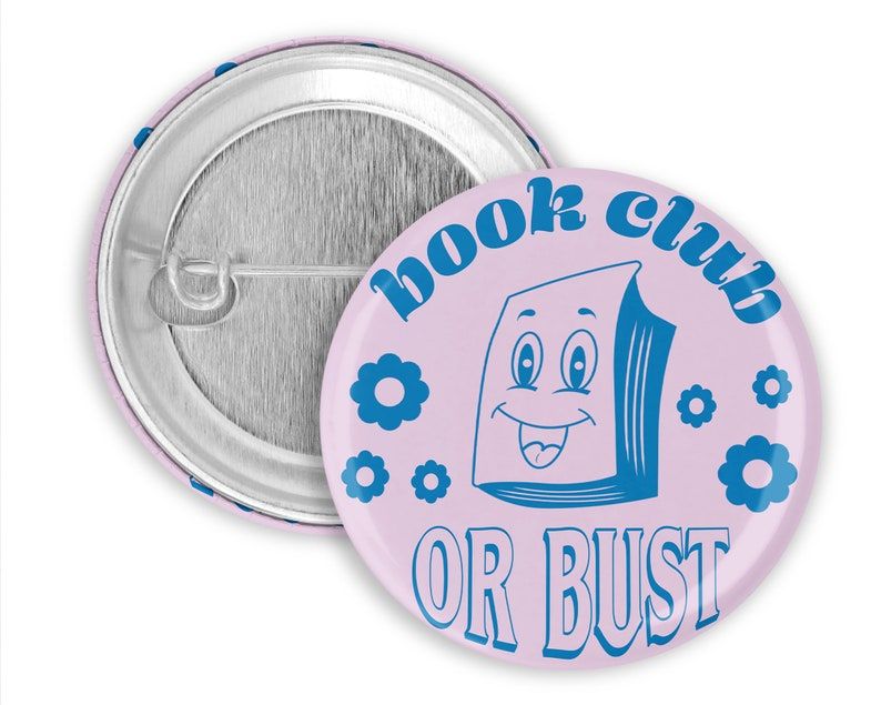Lavender and blue pin that reads "book club or bust" in vintage font. It has a book with a smiling face on it and some flowers. 