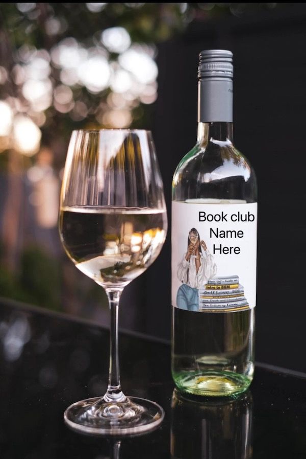 a wine glass filled with white wine next to a bottle with a custom label. The label contains a photo of a Black woman, a pile of books, and text that reads Book Club Name Here