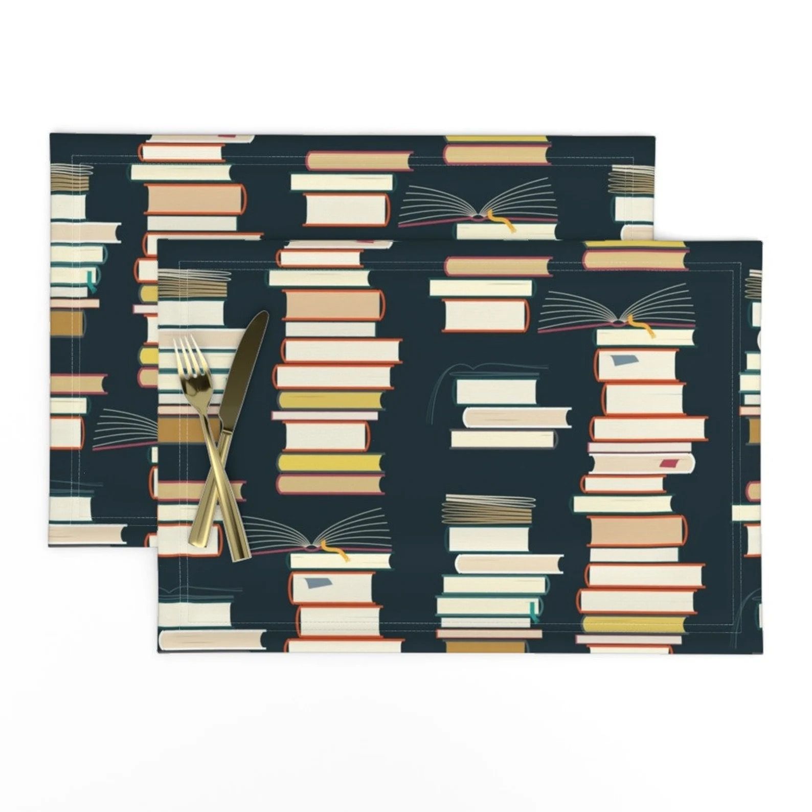 Two black cloth placemats printed with a repeating image of a stack of books.