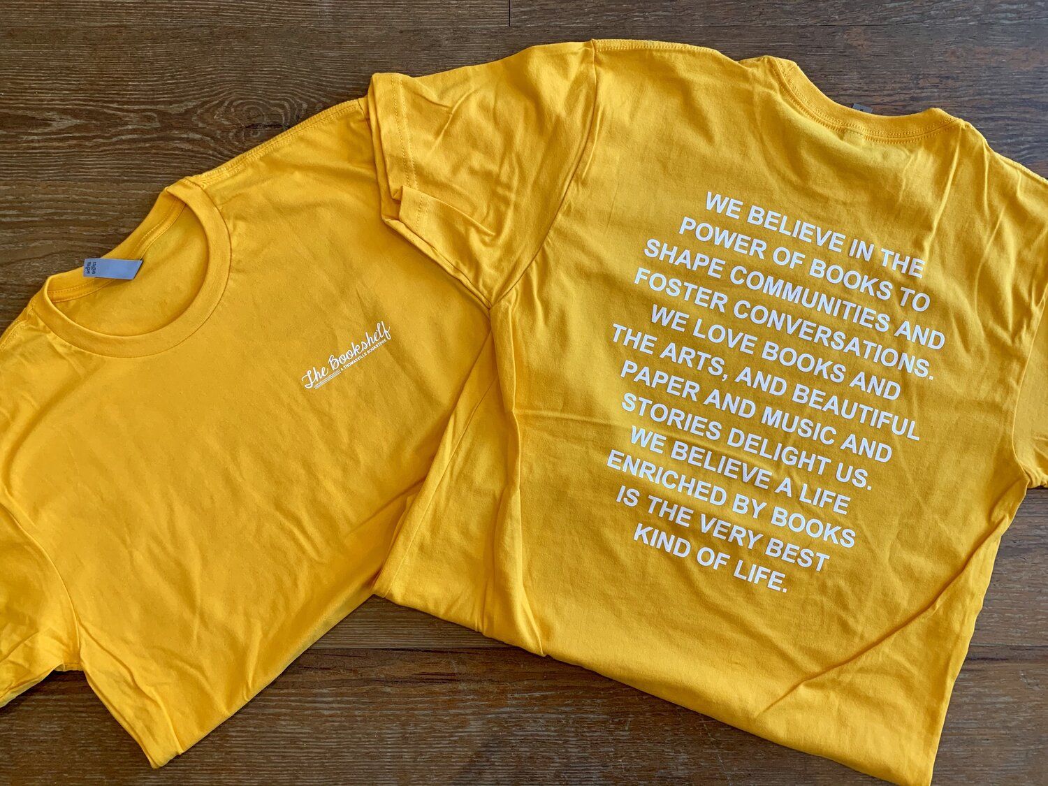 Bright yellow t-shirt with the store's mission statement in white block text