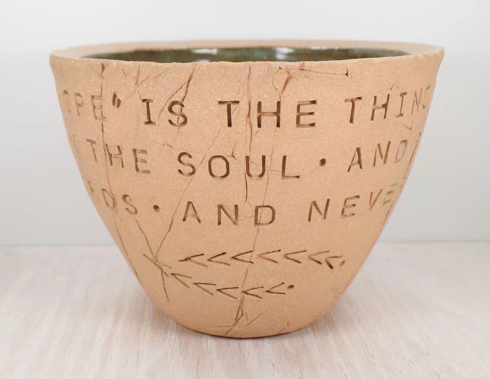 A unglazed ceramic bowl carved with a quote from Emily Dickinson.