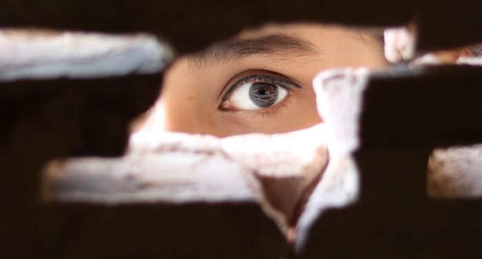 a photo of an eye looking through a gap in a brick wall