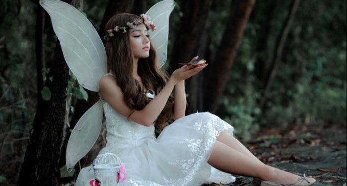 pale skinned woman sitting on the ground dressed in white as a fairy