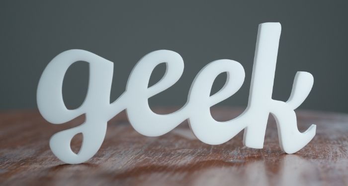 a in white cursive cutout of the word "geek" on a wooden surface