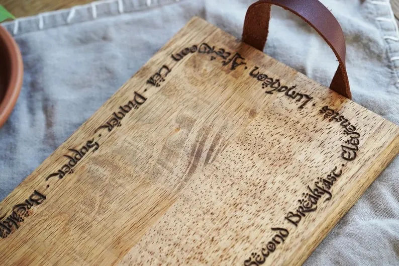 A rectangular wooden cheese board with the names of hobbit meals engraved around the edge in an Elvish script.