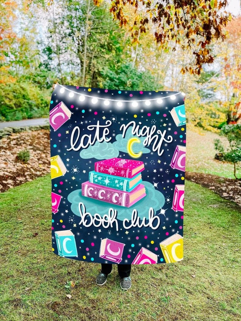 A colorful blanket that reads "late night book club." It's being held in front of a person outside. 