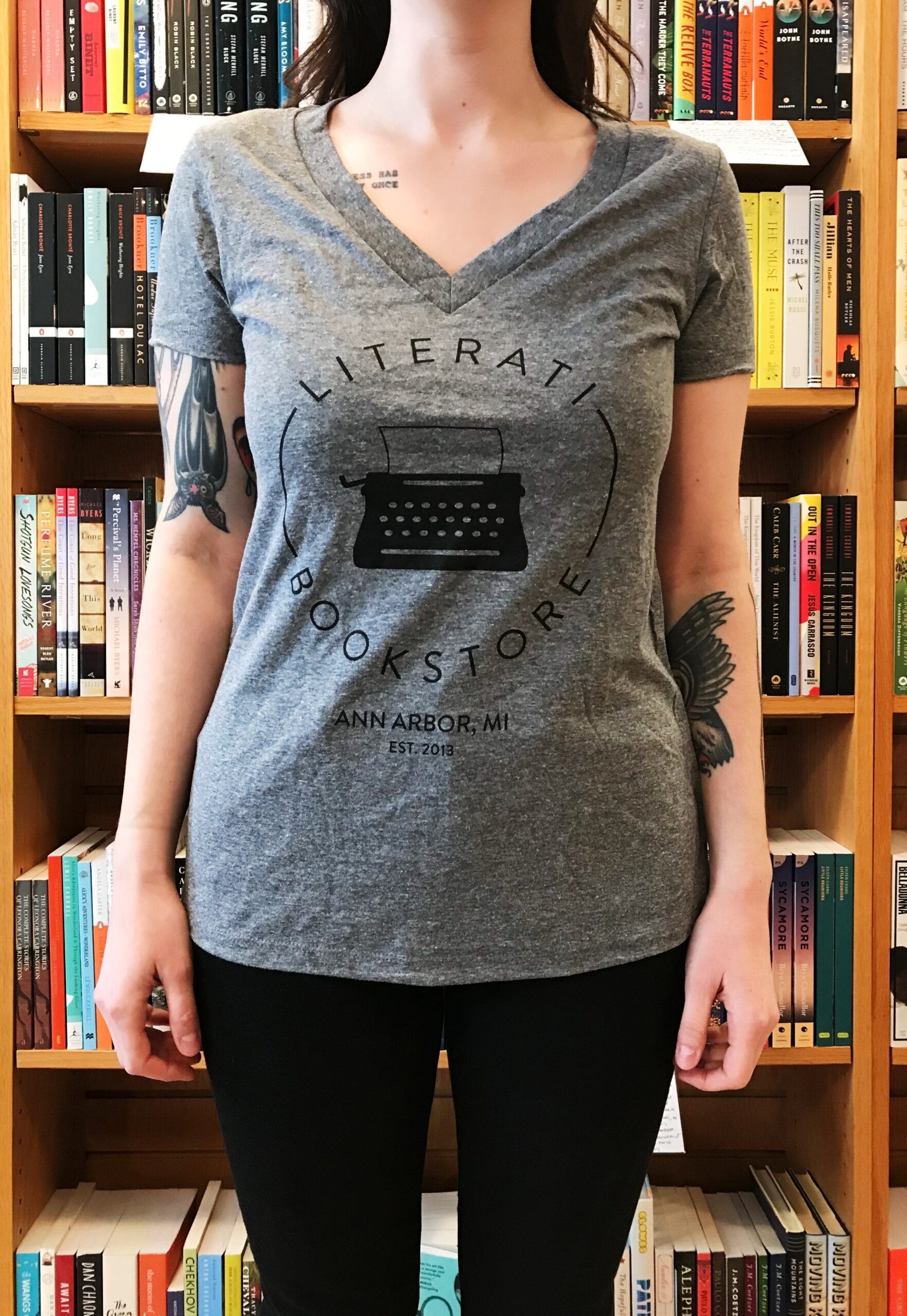 A woman wearing a gray t-shirt that features a typewriter and the words "Literati Bookstore"