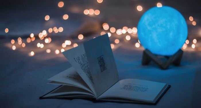 an open book beside a glowing blue orb and twinkle lights in the background