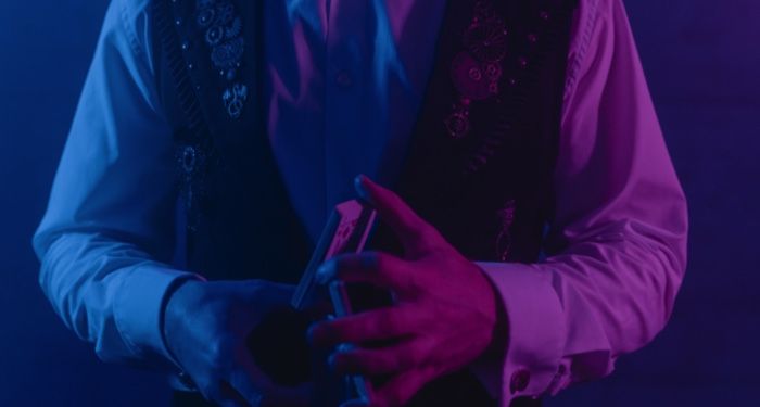 a magician seen from the chest down. In the magician's hands is a deck of cards, image lit in blue and purple light