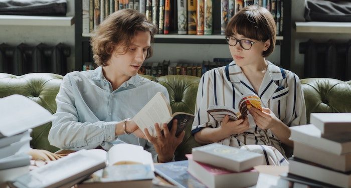 a photo of two people holding books. One is pointing to the book and talking to the other.