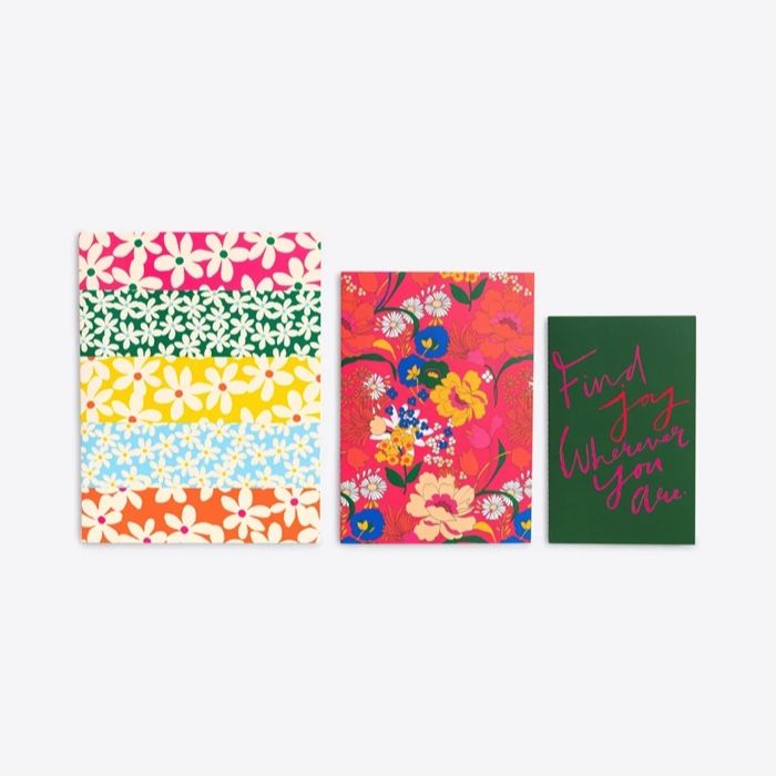a set of three notebooks in ascending sizes; the larger two are floral themed, the small west is green with pink and red text that reads 