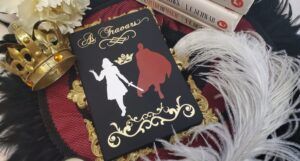 a blac Shades of Magic-inspired hrounel with gold cursive text that reads "As Travars." Beneath the text are a white and red silhouette of the two main characters