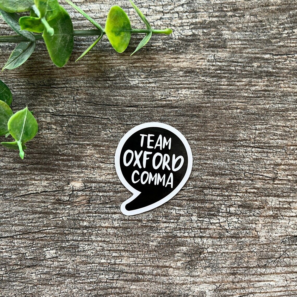 Image of a sticker in the shape of a comma on a tree. It reads "team oxford comma."