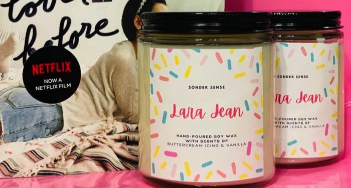 candles with white and confetti decoration that say "Laura Jean" with a copy of To All the Boys I've Loved Before by Jenny Han in the background