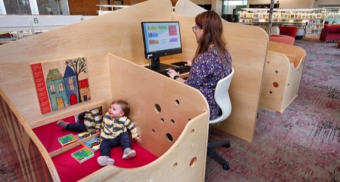 image of a work and play station: a person working at a computer while a small child sits off to the side in an attached secure play area
