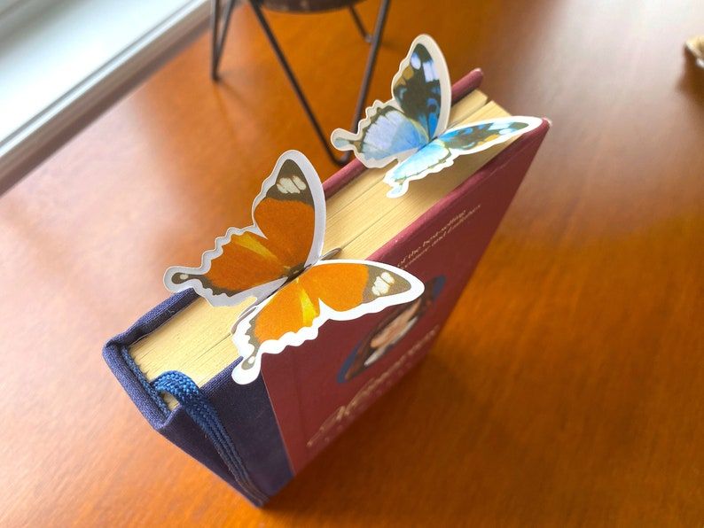 Image of a book standing on its edge. On the top edge are two butterfly bookmarks. 