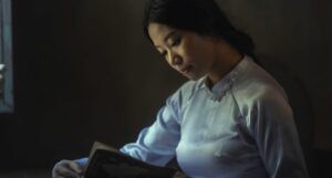 Asian woman reading in dark lighting with a white, satin blouse