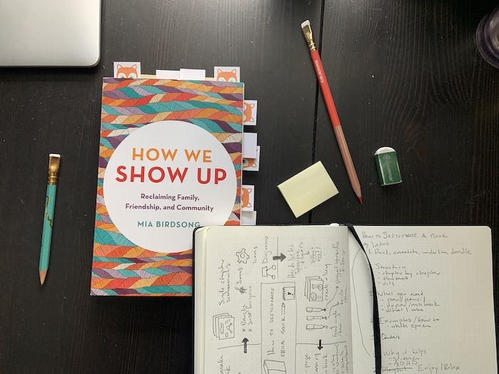 a desk with an open notebook, pencils, and the cover of How We Show Up