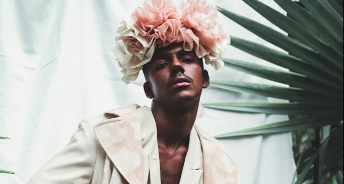 man with dark brown skin wearing a pink rose crown and white clothing posing for the camera