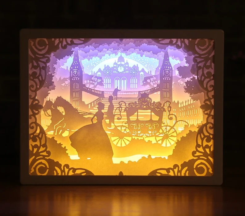 Image of a Cinderella castle scene made of cut paper and illuminated by bright lights. 