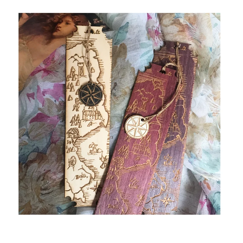 Three wood bookmarks, each of which has a map on it with a tassel featuring a compass. 