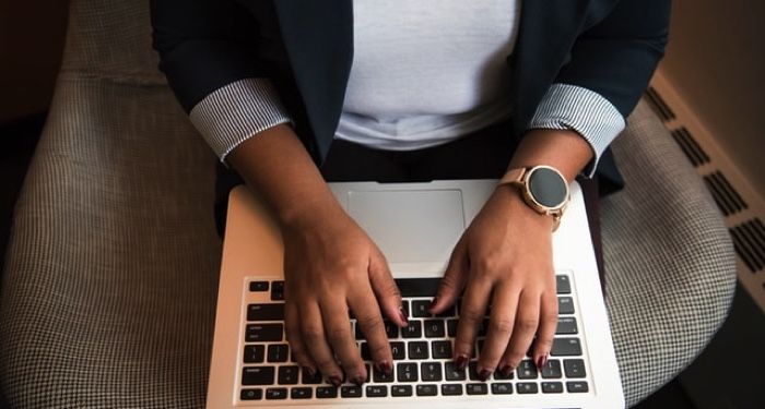 medium brown-skinned hands typing on what appears to be a MacBook laptop