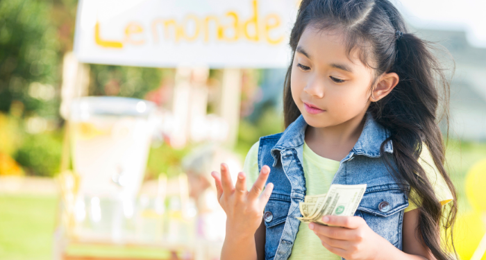 a photo of a kid standing in front a lemonade stand, counting money