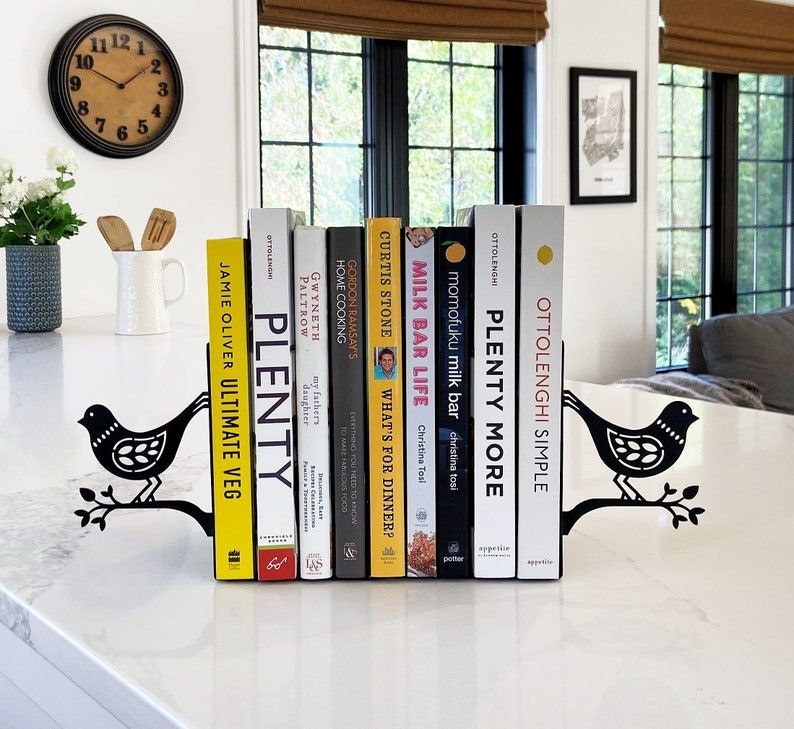 Set of two black metal bookends featuring birds on a branch. They're holding up cookbooks in the image. 