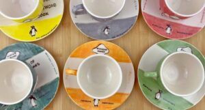 a set of teacups and saucers hand painted to look like Penguin book covers