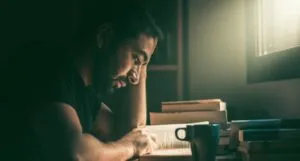 a person with tan skin reading near a window with sunlight pouring in