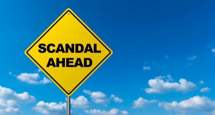 a yellow diamond-shaped sign bearing the words "scandal ahead" against a blue sky