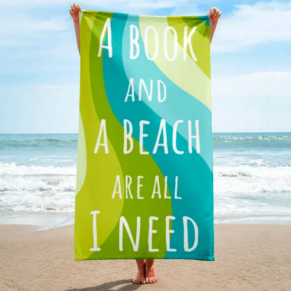 Person on a beach holding up a green and blue beach towel with text "A book and a beach are all I need"