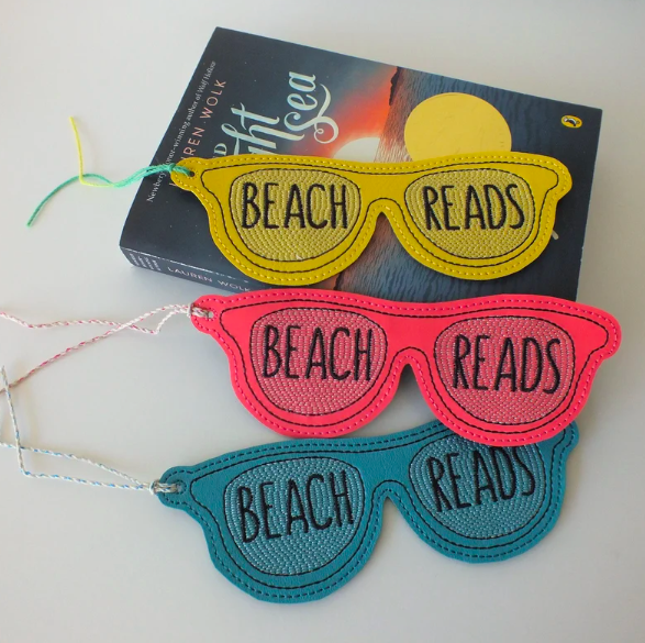 Three fabric bookmarks in yellow, pink, and teal, shaped like sunglasses with 