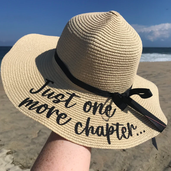 Beige sunhat with black ribbon and black screen printed text that says 