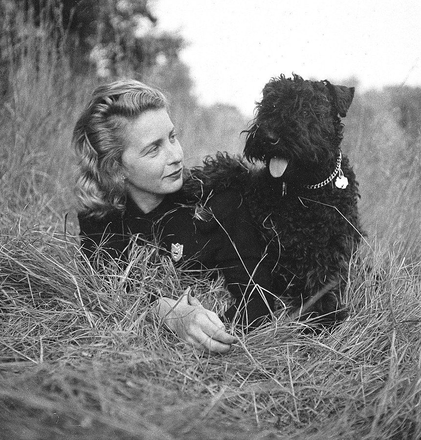 a black and white photo of Margaret Wise Brown lying in grass with a black dog