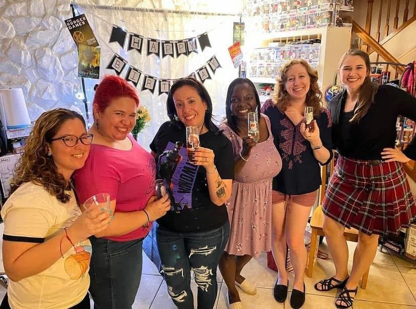a photo of Aurora with her book club friends at a bookish birthday party holding up glasses and smiling