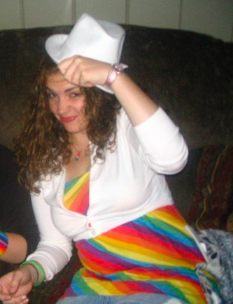 A teenage girl in a rainbow top with a white sweater and hat, looking decidedly uncomfortable and awkward