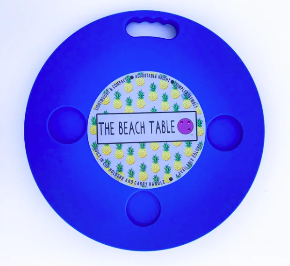 Round blue plastic table with three indents for drinks, handle, and sticker that says "The Beach Table"