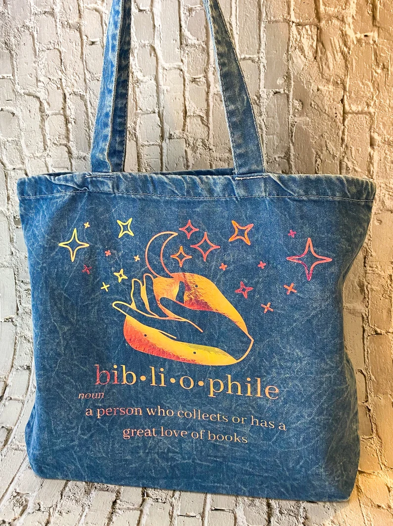 Image of a denim colored tote bag. The screen printing is in yellows, oranges, and reds. It features a hand with stars and reads 