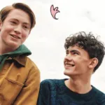 still of the two main characters of Hearstopper smiling at each other as cartoon leaves fall around them