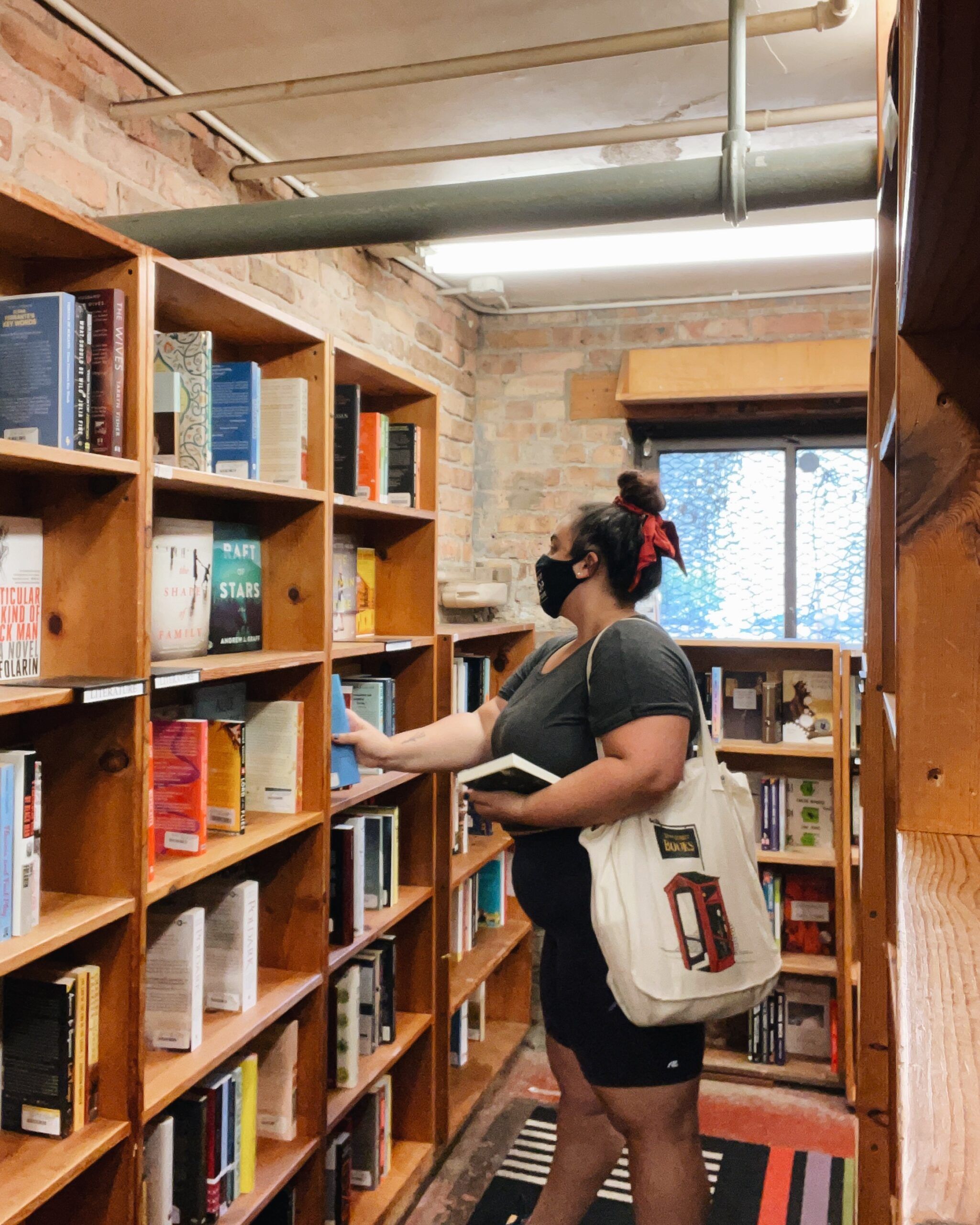 A photo of woman choosing a book off a bookshelf at a bookstore