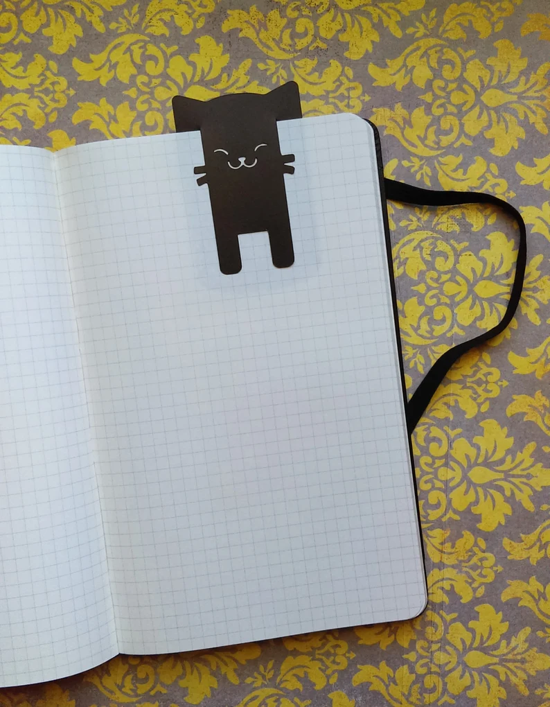 Image of a small bookmark featuring a black cat at the top of a grid notebook. 