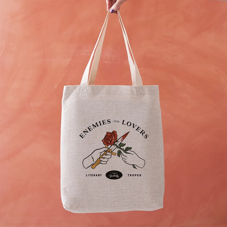 Image of a canvas tote against a coral background. The tote features two hands, one with a knife and one with a rose. It reads 