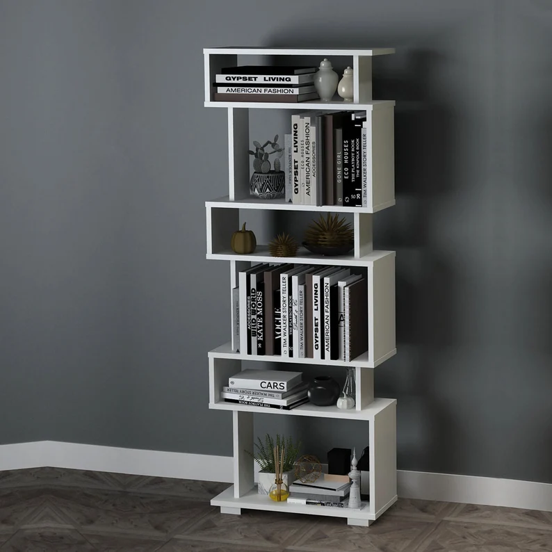 Image of a white bookshelf with six shelves in a geometric pattern. It is against a grey wall. 